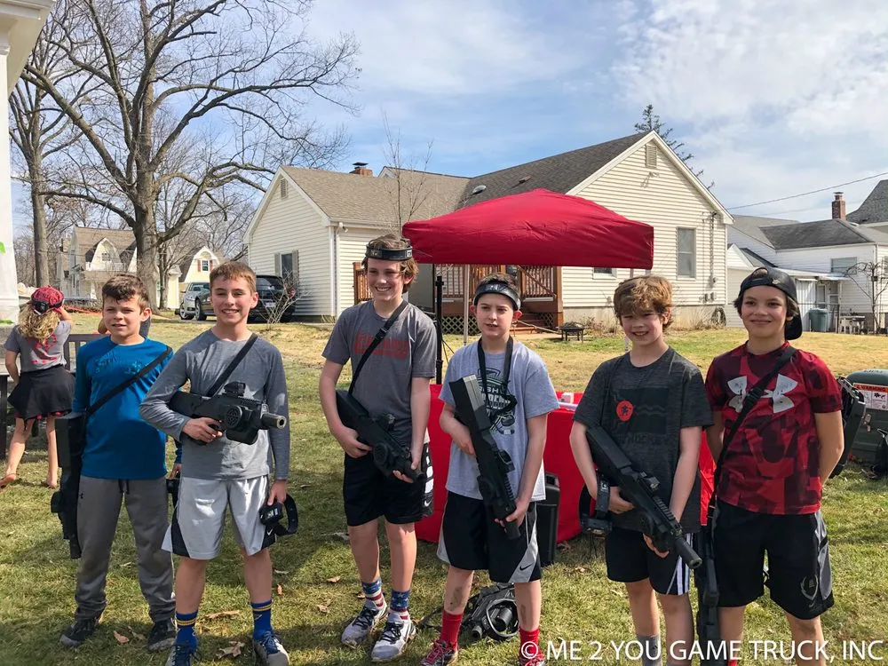 Six kids in headsets holding laser taggers in an ordinary suburban backyard, with neighboring houses behind them